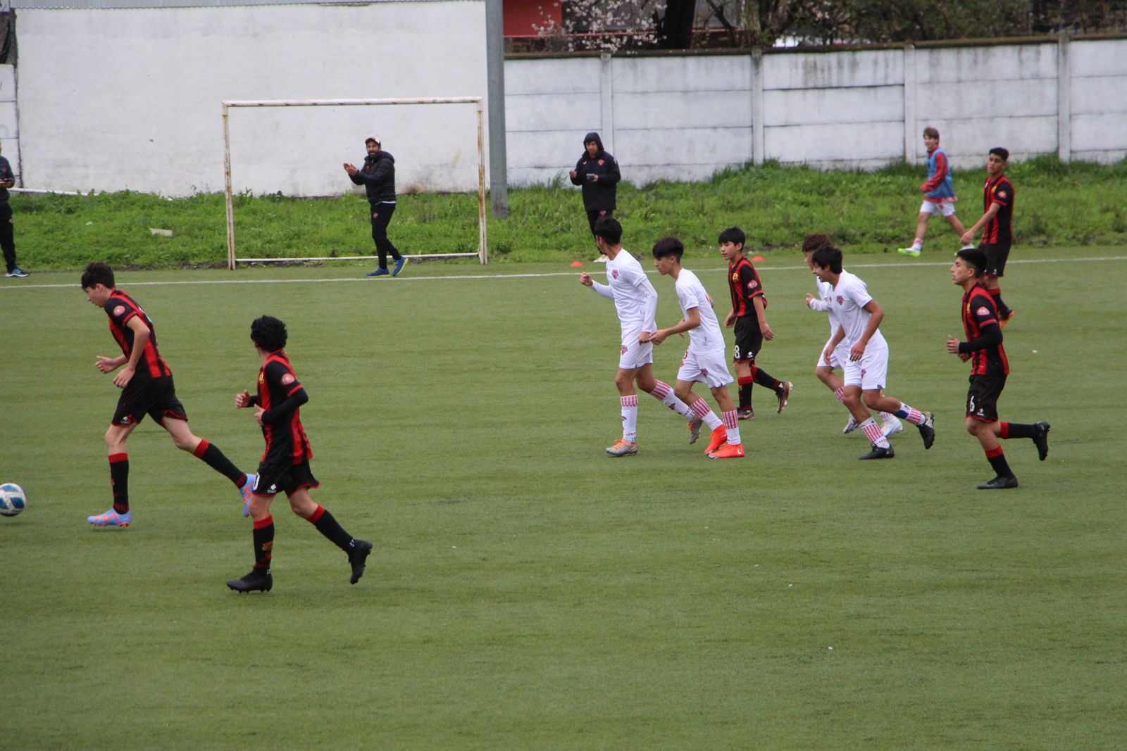 Partido de fútbol juvenil con el cuerpo técnico observando desde el borde de la cancha